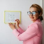 Motywowanie nauczycieli bez premii: narzędzia, które działają w polskich realiach Uśmiechnięta nauczycielka w różowej marynarce pisze Back to School na tablicy